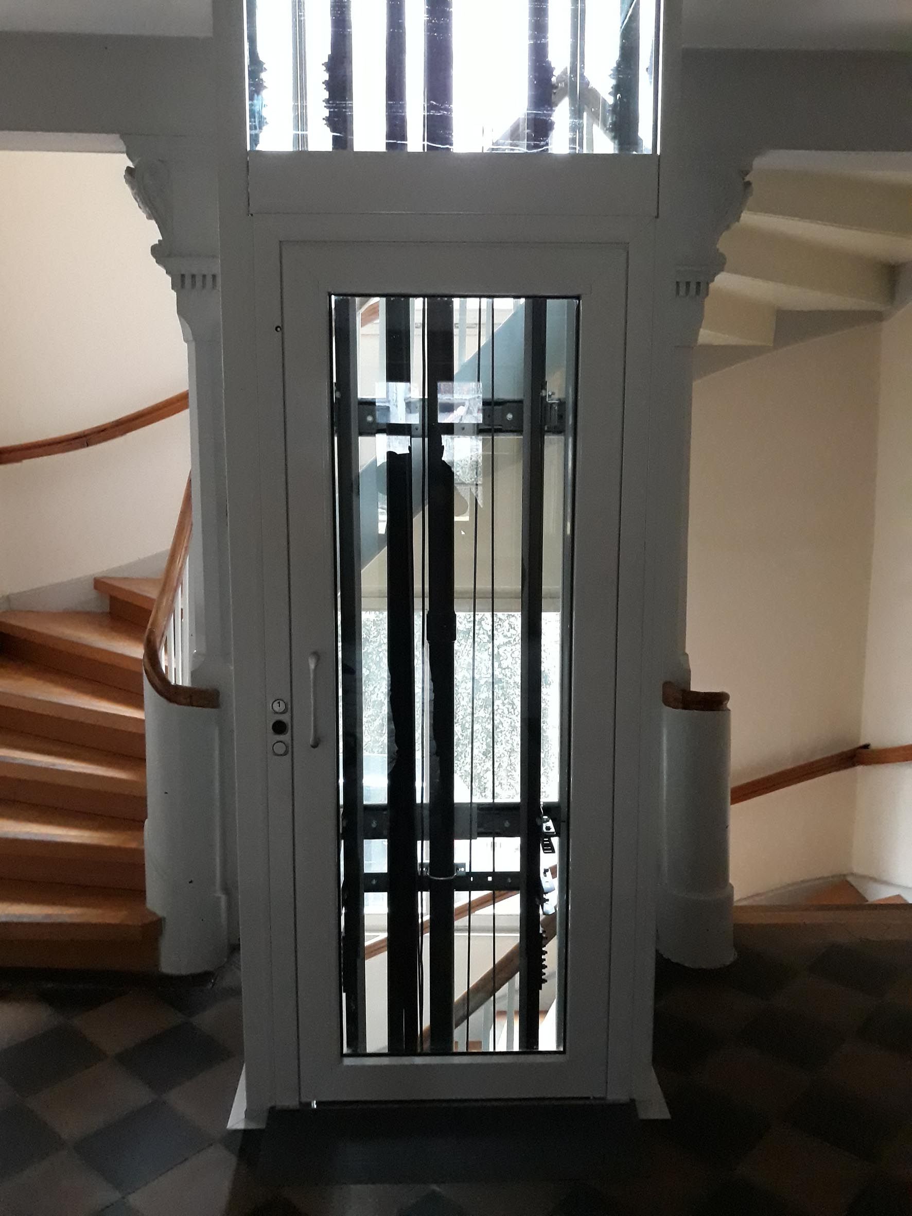 Glaskabine des Aufzugs neben der umgebauten Holztreppe